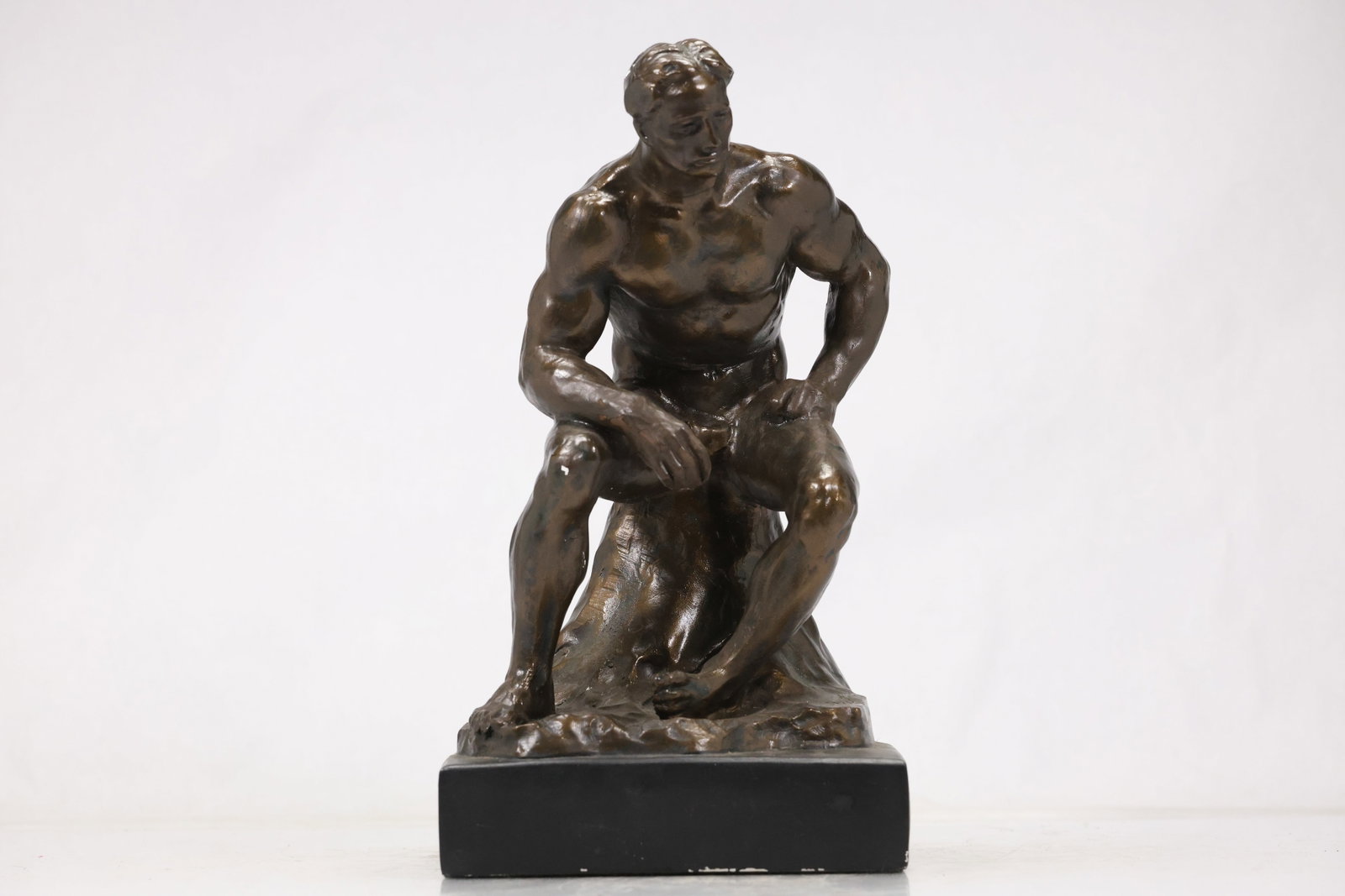 S Eylander AVA 1994 Seated Male Figure Sculpture: Bronze tone figurative sculpture of a muscular seated man leaning forward with one arm resting across a raised knee. The textured surface is inscribed AVA copyright 1994 and S Eylander and the figure 