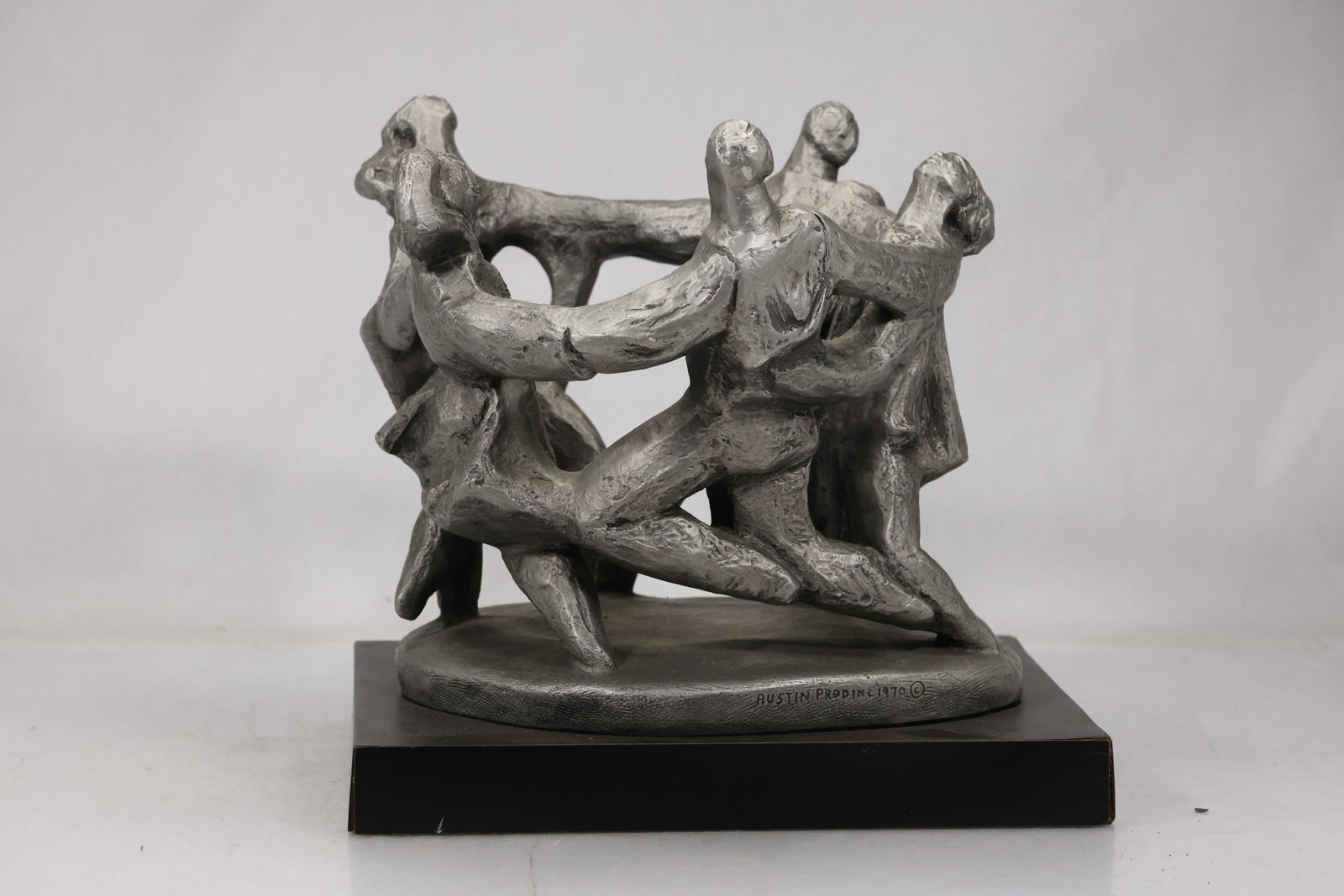 Austin Productions Circle Dance Figural Sculpture: Austin Productions figural sculpture depicting a circle of stylized dancers holding hands around an open central space. The gray stone tone group is mounted on a stepped black base and stamped Austin 