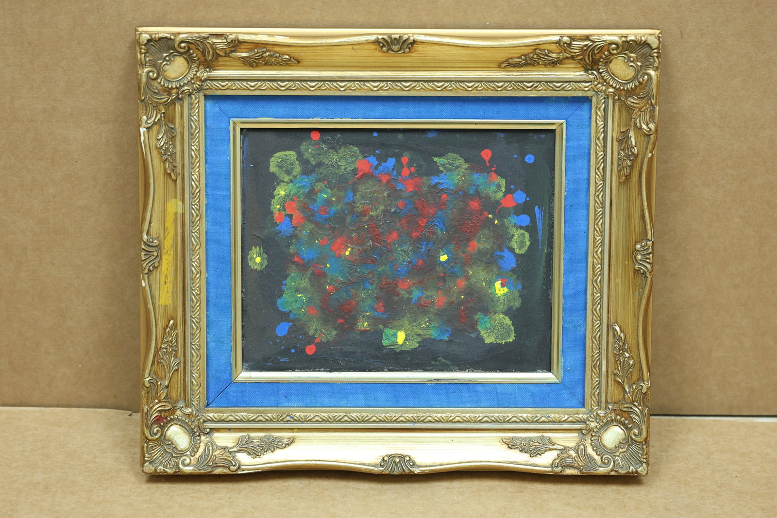 Color Splash Abstract Painting on Black Ground: Framed abstract painting with red blue green and yellow splashes across a black ground. A reverse inscription appears to read The Fake or The Face but is not fully legible. The gestural surface relate