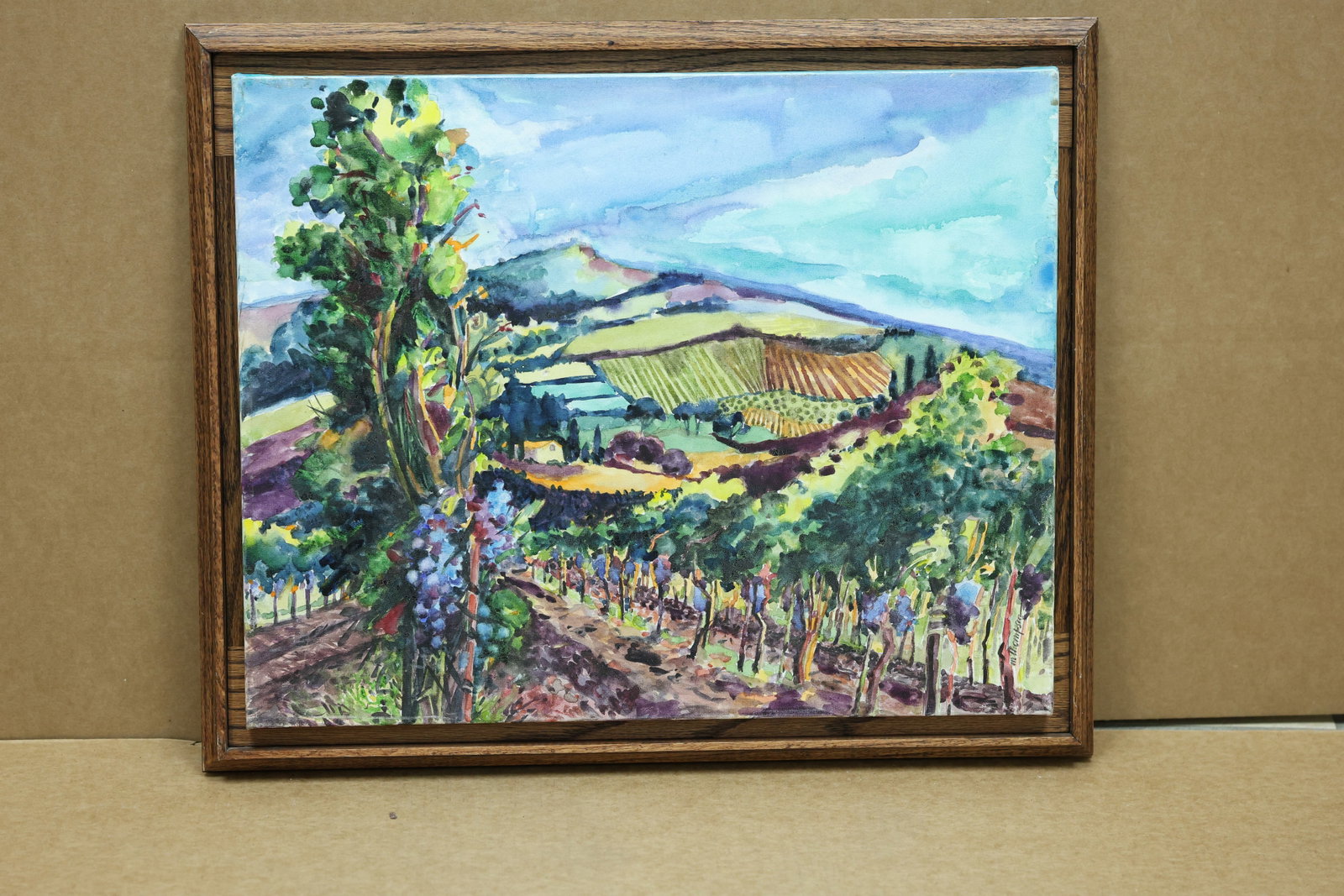M Thompson Colorful Vineyard and Farmland Painting: Framed landscape painting depicting patterned vineyards fields and distant hills in vivid colors. The work is signed M Thompson. The broken color and atmospheric handling relate to Impressionist lands
