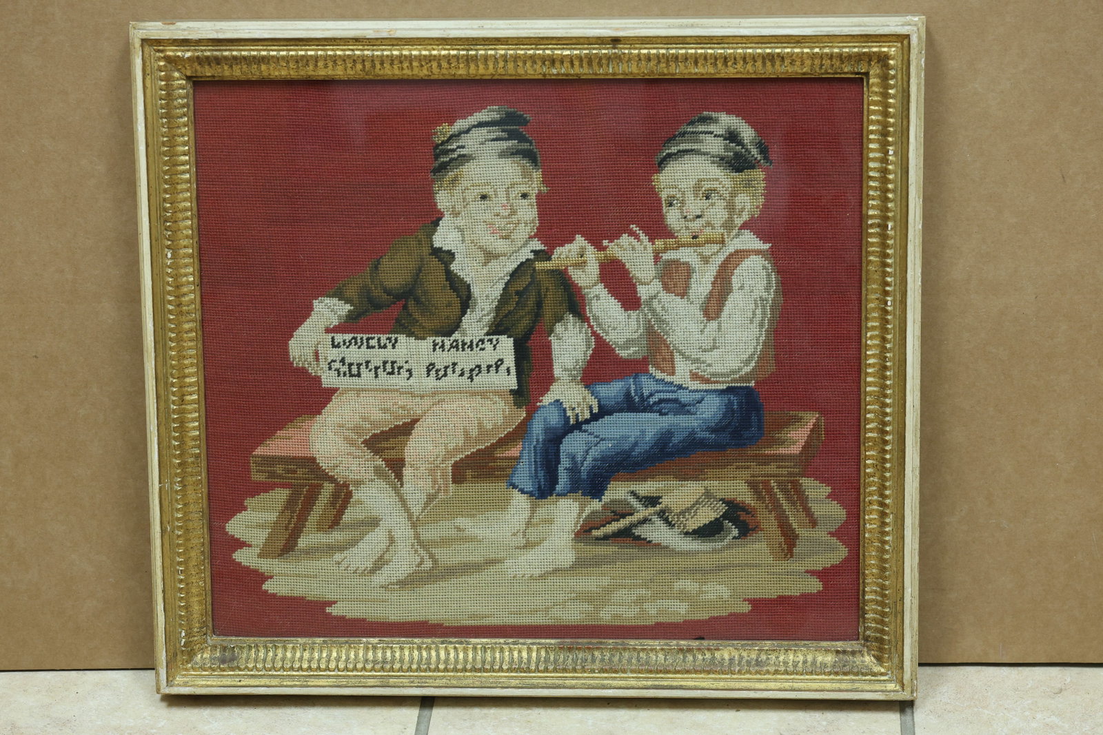 Lindsey and Nancy Children Reading Needlepoint: Framed needlepoint depicting two children reading together. Stitched text includes the names Lindsey and Nancy and may include Saturday Picture. The stitched image relates to Arts and Crafts needlewor