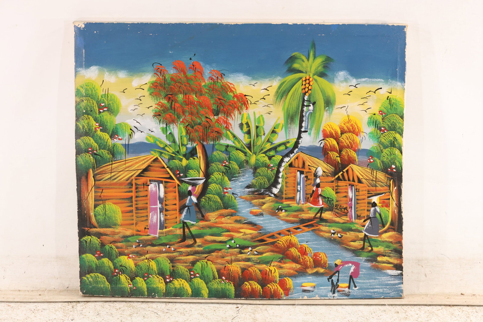 Signed Ronald Haitian Folk Village Oil Painting: Colorful oil painting signed Ronald depicting a Haitian village with houses palm trees figures and cultivated fields. The scene is built from bright flat passages and tightly patterned detail. The ele