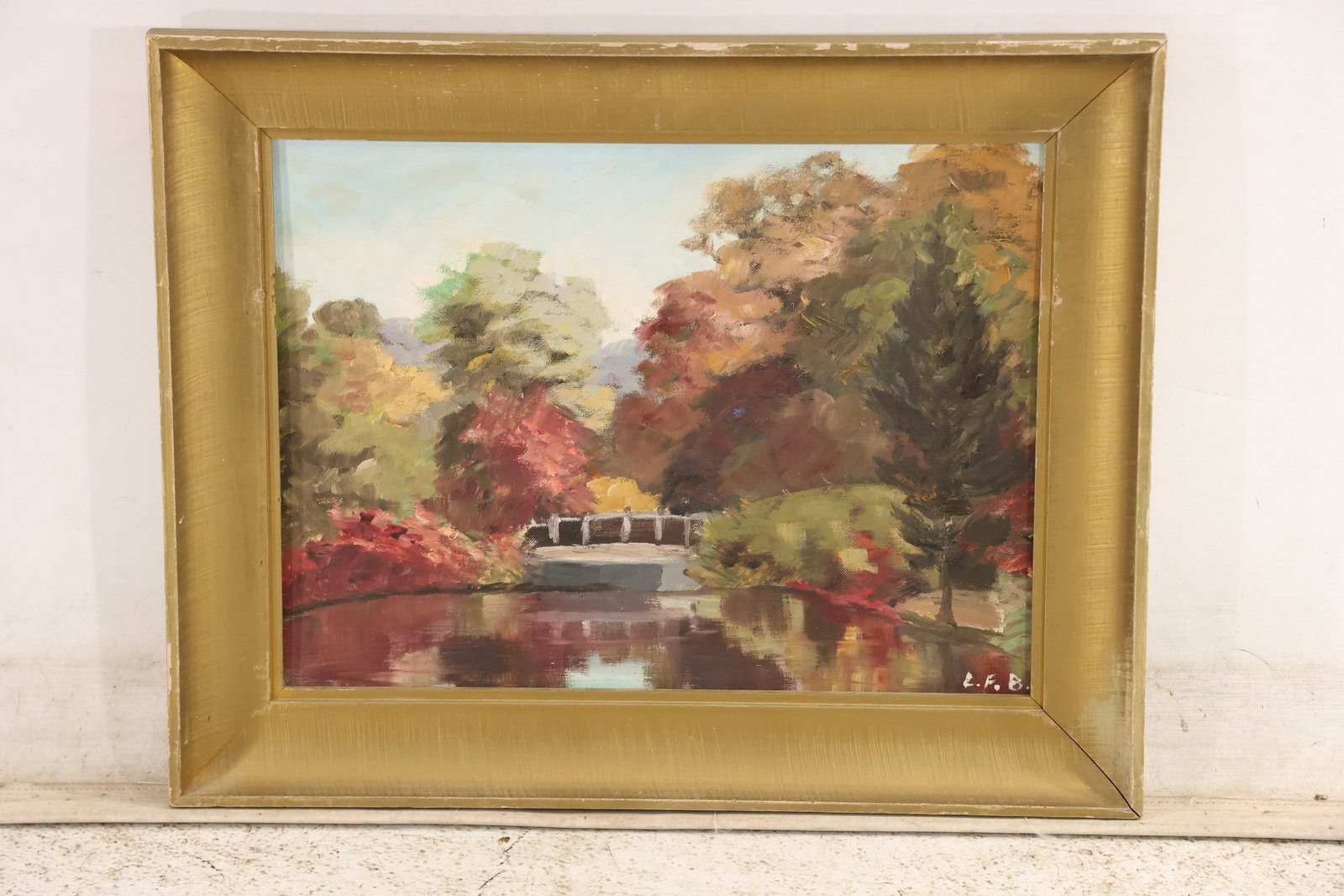 Signed LFB Autumn Landscape Painting on Board: Original landscape painting on board signed with the initials LFB at the lower right. The scene depicts a pond bridge and autumn trees in red gold and green within a gilt frame. The reflective water
