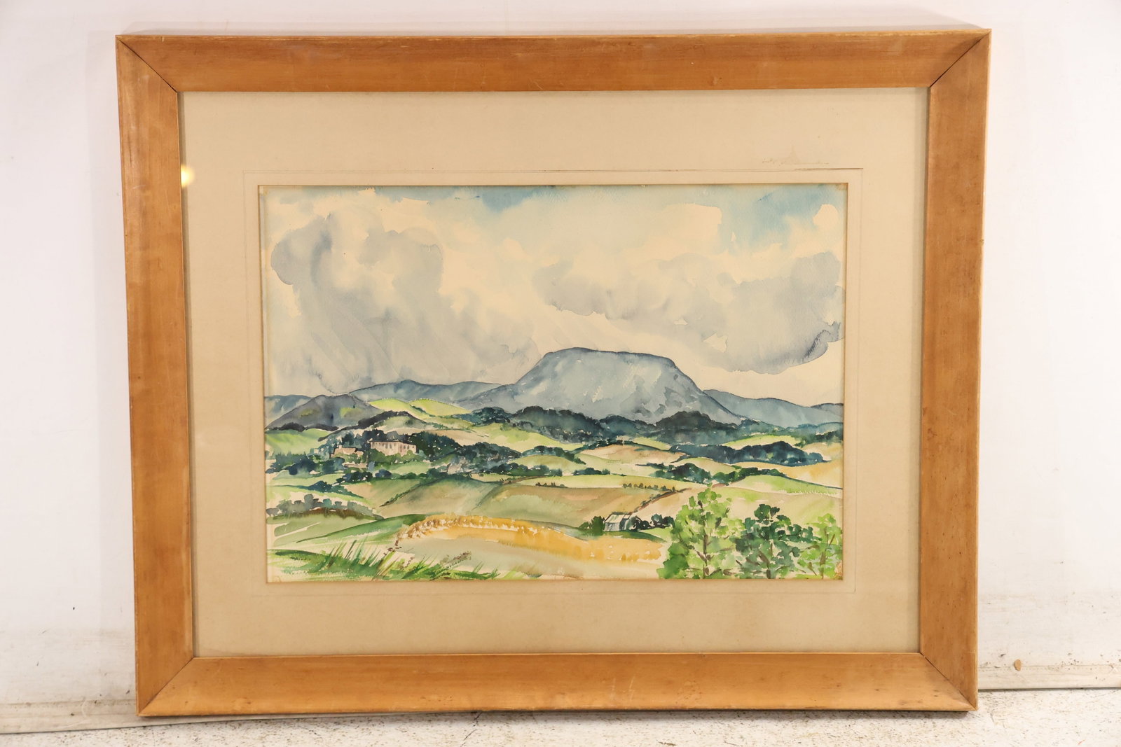 Unsigned Mountain Valley Landscape Watercolor Painting: Unsigned original watercolor on paper depicting a broad green valley with distant blue mountains and pale sky. The scene is framed under a wide mat in a natural wood frame. The transparent washes and 