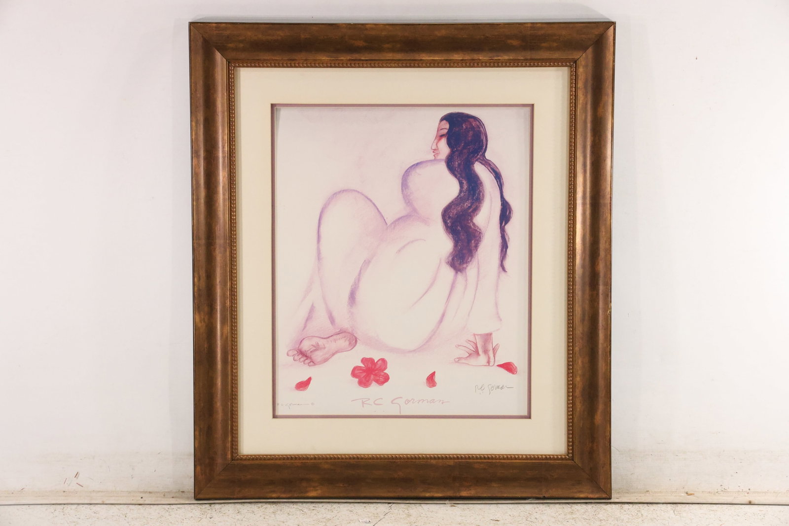 Signed R C Gorman Seated Woman with Flowers Print: Framed fine art print by Navajo artist R C Gorman 1931 to 2005 depicting a seated woman with flowing dark hair and pink flowers scattered around the figure. The work is signed in pencil and presented 