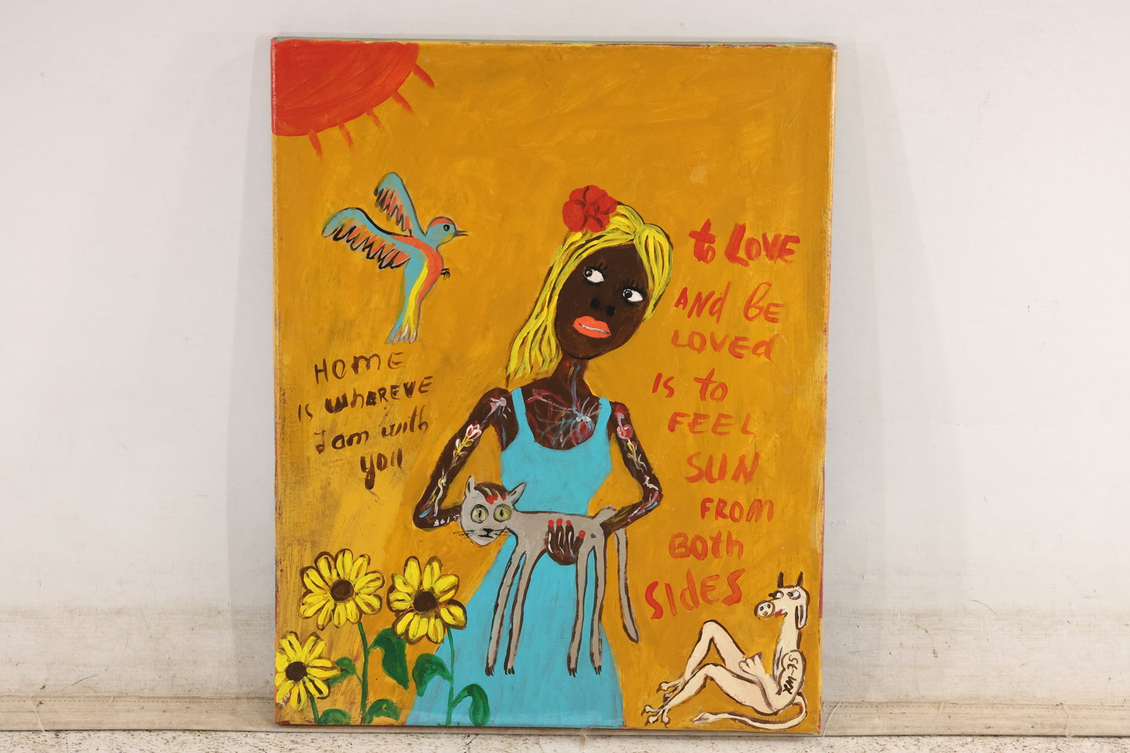 Folk Art Painting of Woman with Cat, Marked XM-75: Colorful painting on canvas depicting a woman holding a cat, with sunflowers, a bird, a sun, and a dog. Includes the phrases “Home is wherever I am with you” and “To love and be loved is to 