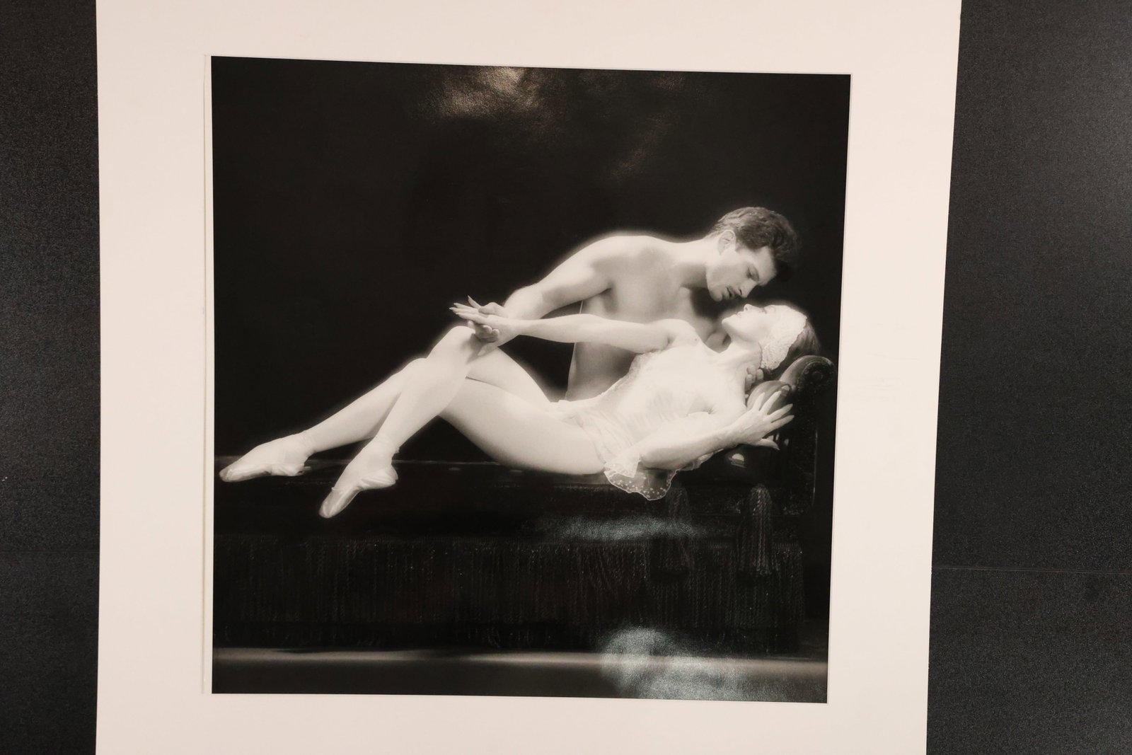 Black-and-White Photograph of Two Reclining Figures: Photographic print depicting two intertwined reclining figures against a dark background. Presented with a wide light-colored mat. Size: Outside mat: 25 x 25 inches. Shelf ID: mc1 **Pickup Notice:** T
