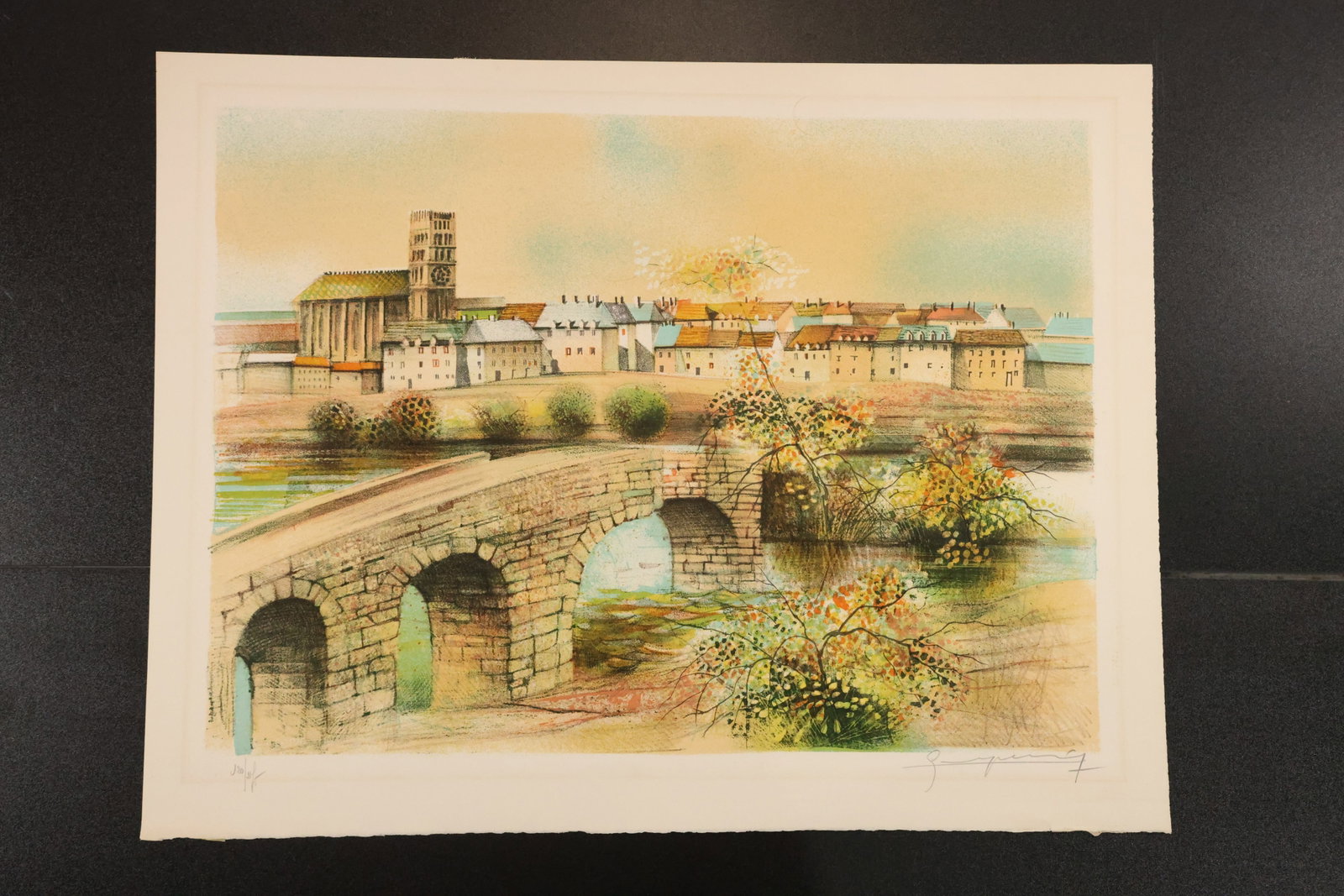 Signed French Town and Stone Bridge Lithograph: Color lithograph depicting a stone bridge beneath a French town with towers and closely grouped buildings. Signed in pencil in the lower margin. Size: 20 x 26 inches. Shelf ID: mc1 **Pickup Notice:** 