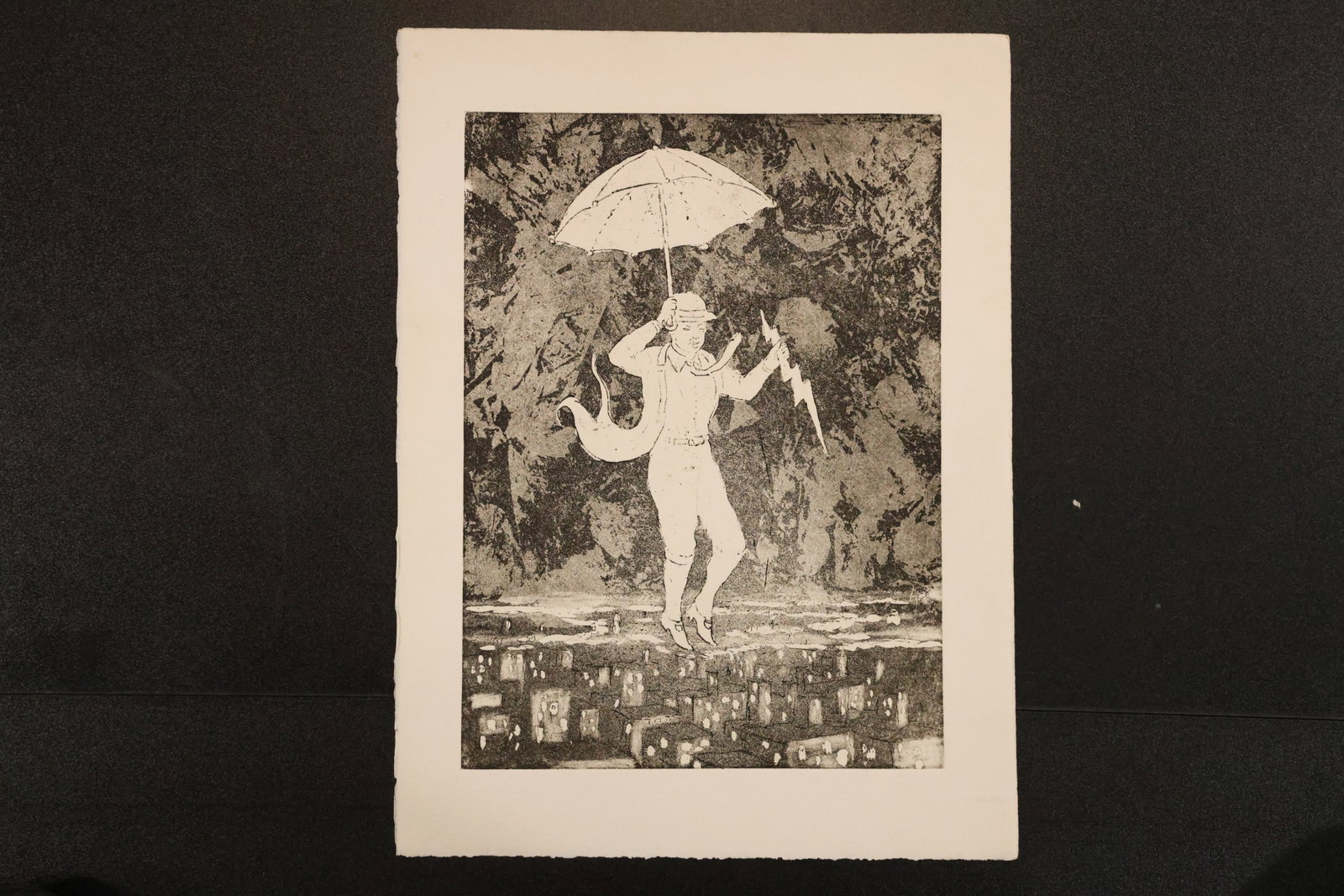 Figure with Umbrella Black-and-White Etching: Etching on paper depicting a figure holding an umbrella above a dark cityscape, with a jagged lightning-like form at one side. Size: 15 x 11 inches. Shelf ID: mc2 **Pickup Notice:** This item requires