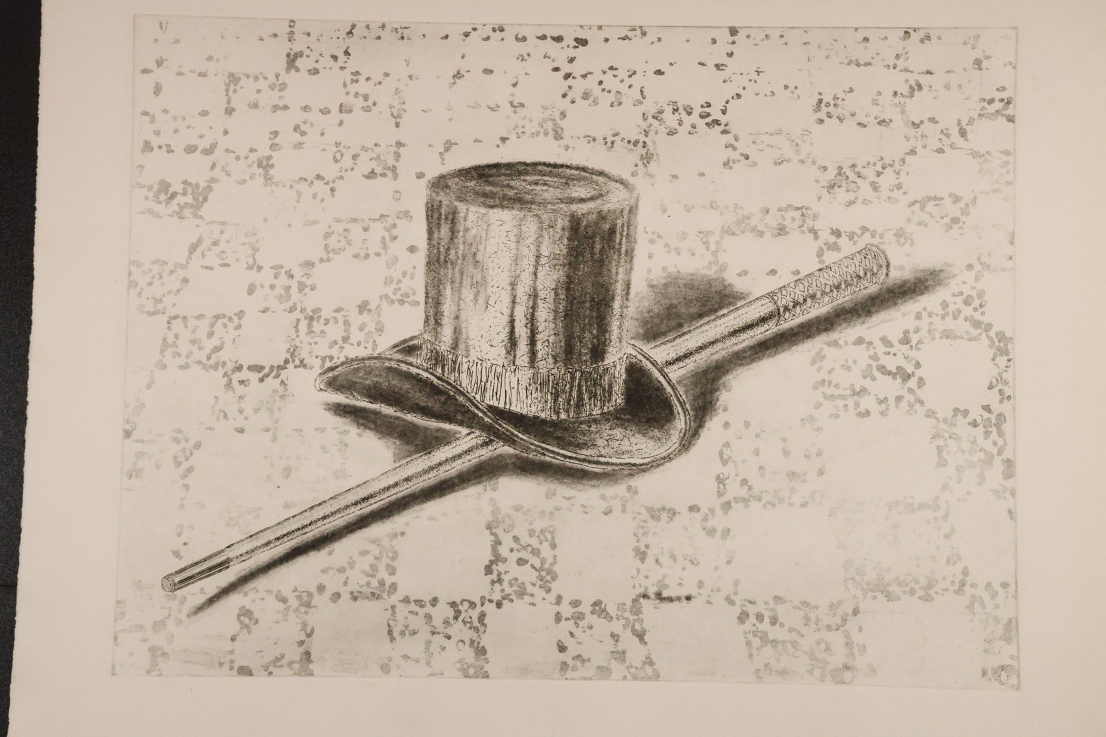 Magician’s Top Hat and Wand Black-and-White Print: Black-and-white print depicting a top hat and wand against a lightly patterned background. Fine lines and crosshatching define the hat and its shadow. Size: 22 x 30 inches. Shelf ID: mc2 **Pickup Noti