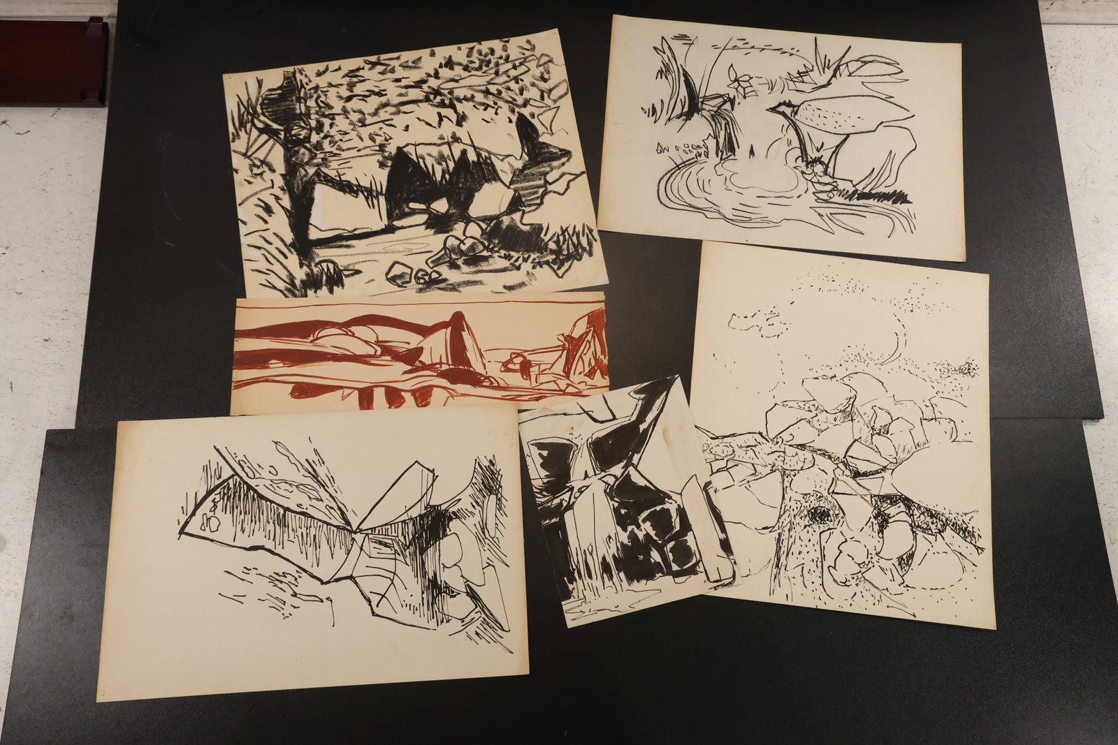 R. Angeloch Group of Black and Red Landscape Drawings: A group of drawings on paper by R. Angeloch, including wooded scenes, angular structures, and abstract natural studies. Most are in black, with a red landscape also included. Size: 14 x 17 inches. She