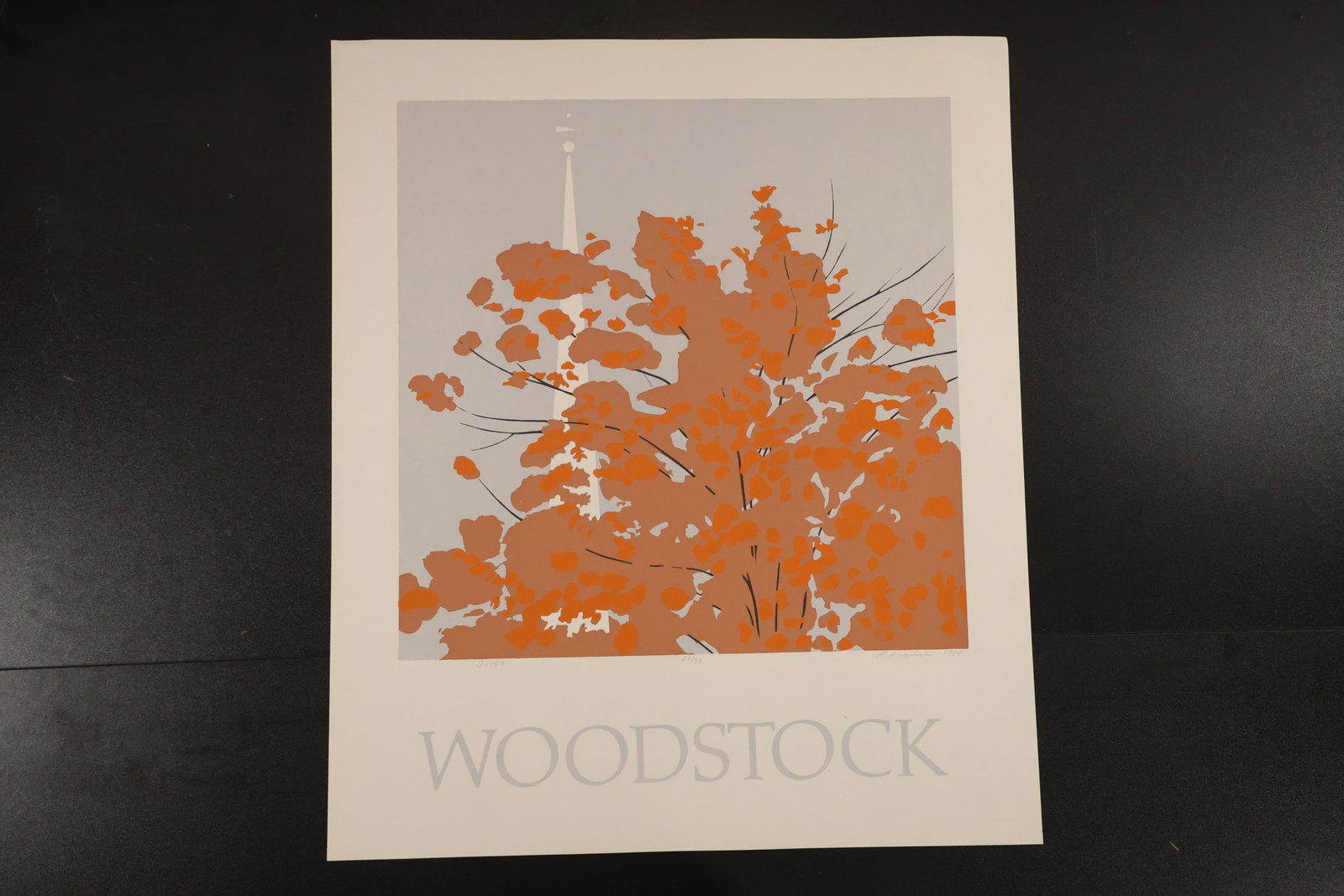 R. Angeloch Woodstock Orange Foliage Print: A color print by R. Angeloch featuring bright orange foliage, fine dark branches, and a pale church steeple against gray. The word WOODSTOCK appears below the image. Size: 26 x 22 inches. Shelf ID: mc