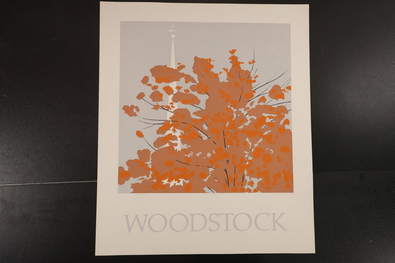 R. Angeloch Woodstock Autumn Foliage Color Print: A color print by R. Angeloch featuring orange foliage and a slender pale steeple against a gray ground. WOODSTOCK appears below the image on the light lower margin. Size: 26 x 22 inches. Shelf ID: mc4