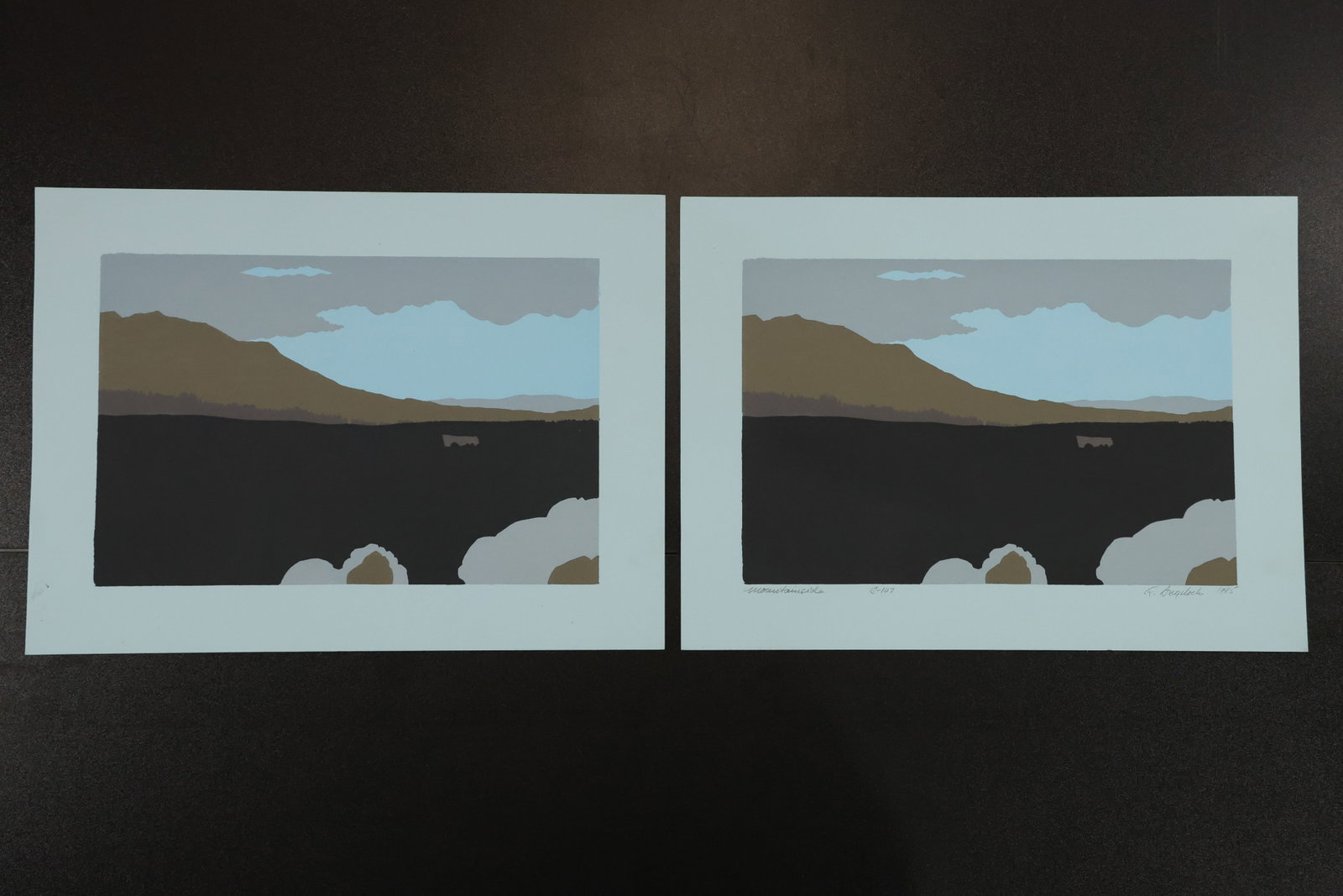 R. Angeloch Pair of Blue Paper Landscape Prints: A pair of landscape prints by R. Angeloch on blue paper, one cataloged as signed. Each depicts a dark foreground, distant brown hills, and pale blue sky beneath gray clouds. Size: 11 x 15 inches. Shel