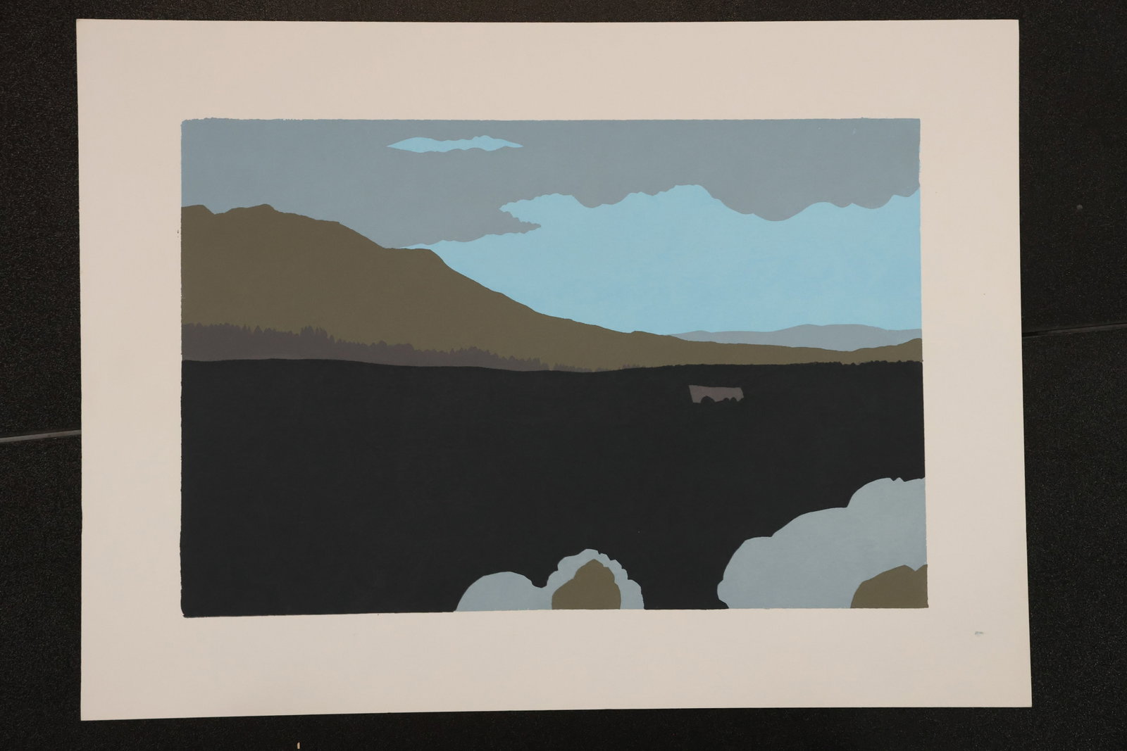 R. Angeloch Mountain and Water Landscape Color Print: A color print by R. Angeloch on white paper. A dark expanse of water lies below brown hills and a blue sky crossed by gray clouds, with pale rocks along the foreground edge. Size: 11 x 15 inches. Shel