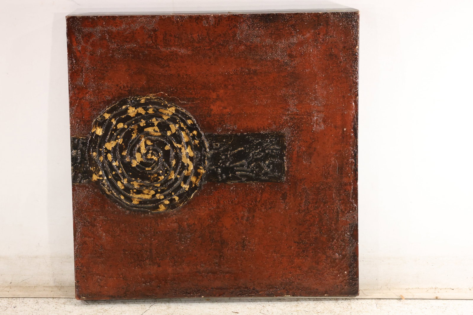 Velázquez Signed Textured Spiral Relief Painting: A mixed-media relief painting with a raised spiral medallion and horizontal dark bar against a mottled rust-red ground. Gold-colored highlights accent the heavily textured forms. Bears a signature on 
