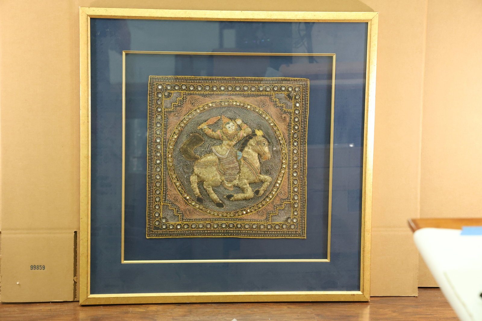 Kalaga Style Embroidered Horse and Rider Textile Panel: Square embroidered textile panel with a central horse and rider inside a circular medallion. Gold tone thread, beads and sequins outline the figure and patterned border against a dark ground. The ride