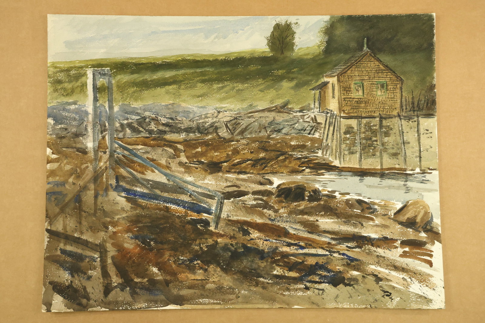 Small Shore Building and Rocky Inlet Watercolor Attributed to Franklin Shores: Watercolor on paper depicting a small brown building beside exposed rocks and shallow water. Blue gray timber rails cross the foreground, with a grassy bank and stone wall behind. Unsigned in the supp