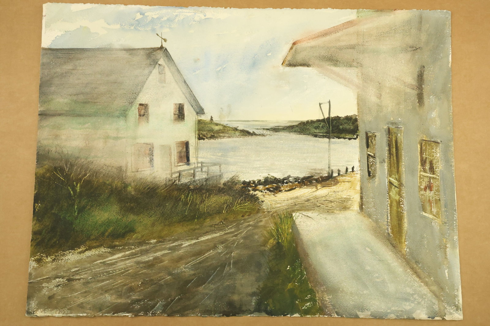 Coastal Lane between White Buildings Watercolor Attributed to Franklin Shores: Watercolor on paper showing a lane between pale buildings leading toward a waterfront. A projecting roof and windows frame the right side, with grasses and rocky ground below. Unsigned in the supplied