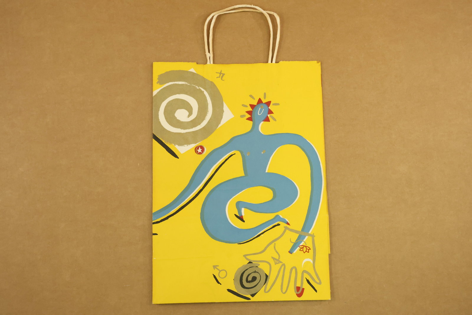 Bloomingdales Yellow Shopping Bag with Swirling Figure Design: Printed paper shopping bag with cord handles and a yellow ground. A blue twisting figure and spiral motifs decorate one side, with a red figure on the reverse. The base carries Bloomingdales and Equit