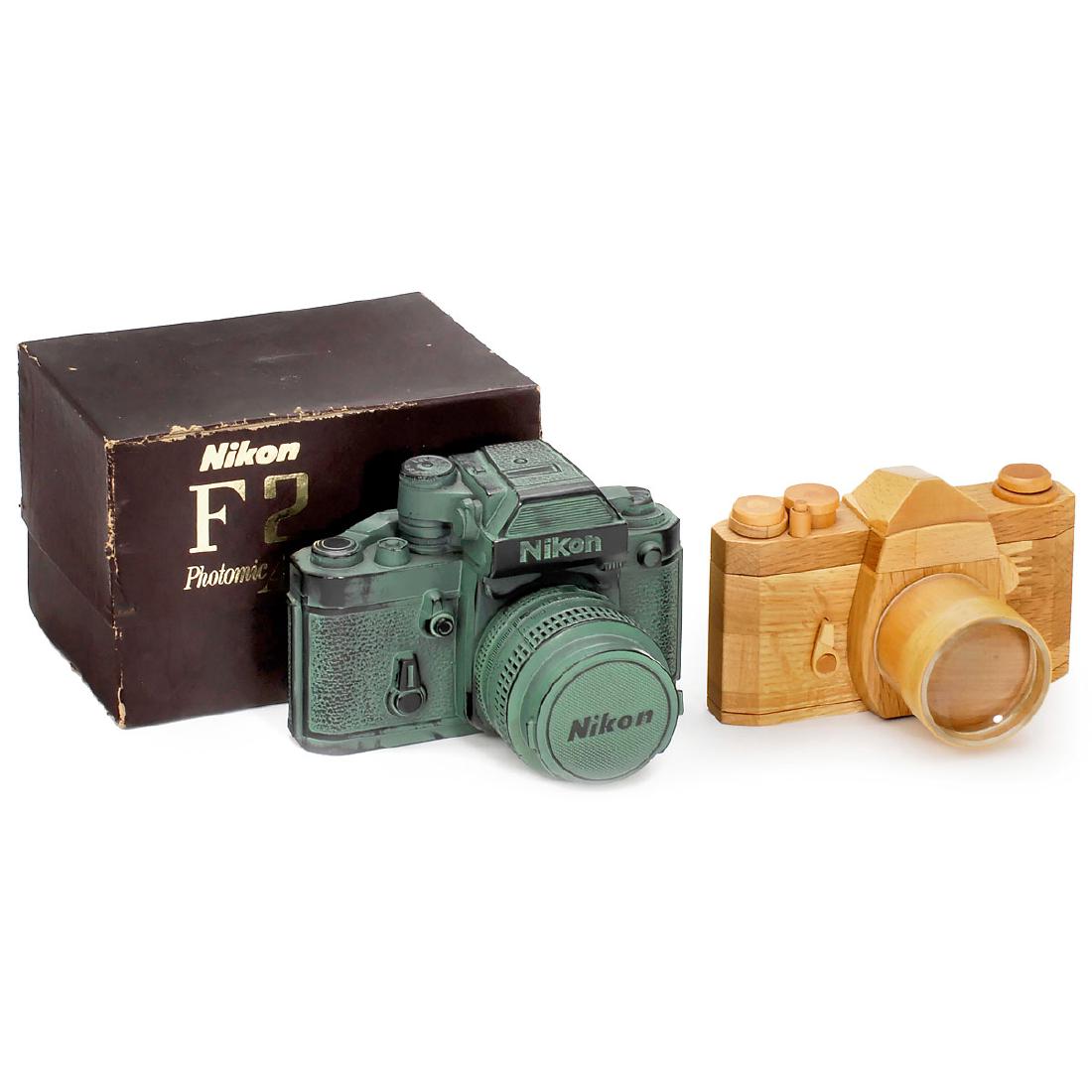 "Nikon F2" Money Bank and Wooden Camera: "Nikon F2" Money Bank and Wooden Camera 1) "Nikon F2 Photomic AS" money band, all-metal, "lens" removable, with original box. – And: 2) Wooden model camera (35mm SLR camera), interchangeable lens (