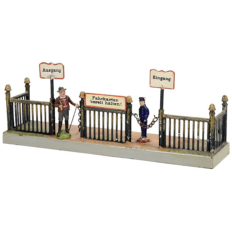 Märklin Gauge I Platform Entrance, c. 1910: Märklin Gauge I Platform Entrance, c. 1910 Hand-painted tin, original signs, 2 composition figures (1 damaged), 10 x 2 ½ in. Märklin Bahnsteig-Sperre Spur I, um 1910 Handlackiertes Blech, Original-