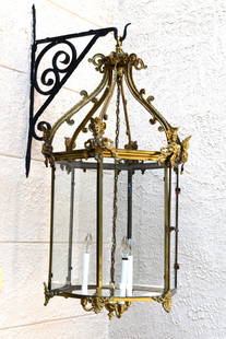 LARGE ORNATE LOUIS XV STYLE BRASS HALL LANTERN: This large and ornate Louis XV style brass hall lantern of hexagonal form. The arched scrolled top with mask and acanthus decorated corners. The six glazed panels with anthemion case terminals. Having