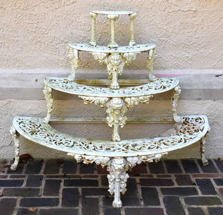 ORNATE VICTORIAN STYLE  FOUR TIER CAST IRON DEMILUNE PLANT STAND: The stand of demilune form with pierced scalloped floral design shelves supported on lion's head and paw legs. Height 37 3/4" Width 48" Depth 25"