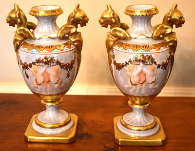 PAIR OF LIMOGE GILT & HANDPAINTED URNS: Of Classical design with gilt griffin head handles with urn formed bodies decorated with relief molded winged cherubs with gilt floral garlands of flowers. The base marked R. Rosier Limoges Décor H