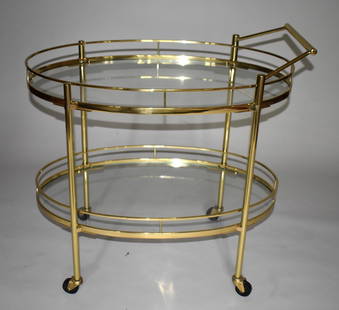 FINE BRASS AND GLASS BAR CART/DESSERT TROLLEY: The trolley of modern design with finely polished and laquered brass body consisting of two oval glass shelves with galleried sides supported by four tubular legs fitted with wheels. Height 30 1'2" De