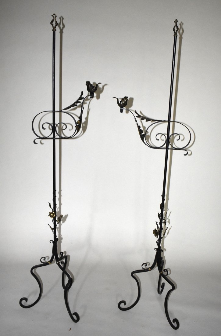 PAIR OF ELABORATE WROUGHT IRON CANDLELAMPS: In the Continental taste, the wrought iron poles with adjustable scroll and acanthus arms with foliate candlecups above brass foliated lower shaft on three arched scroll formed legs. Height 64 1/2"
