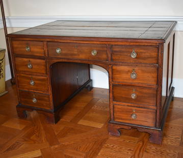 ENGLISH REGENCY MAHOGANY FLAT TOP DESK: The English Regency mahogany desk with brown inset tooled leather top above a central drawer with arched kneehole flanked by banks of four drawers. The case with paneled sides and back on bracket feet