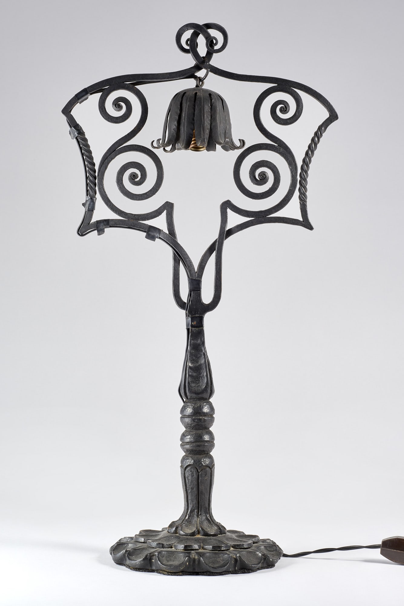 Carlo Rizzarda (Feltre 1883 - 1931) Forged iron lamp. Milan, 1925ca. Base with overlapping scales,: Carlo Rizzarda (Feltre 1883 - 1931) Forged iron lamp. Milan, 1925ca. Base with overlapping scales, baluster-shaped stem and lamp holder ring decorated with spirals, torchons and leaves. (h 47 cm.) Lit