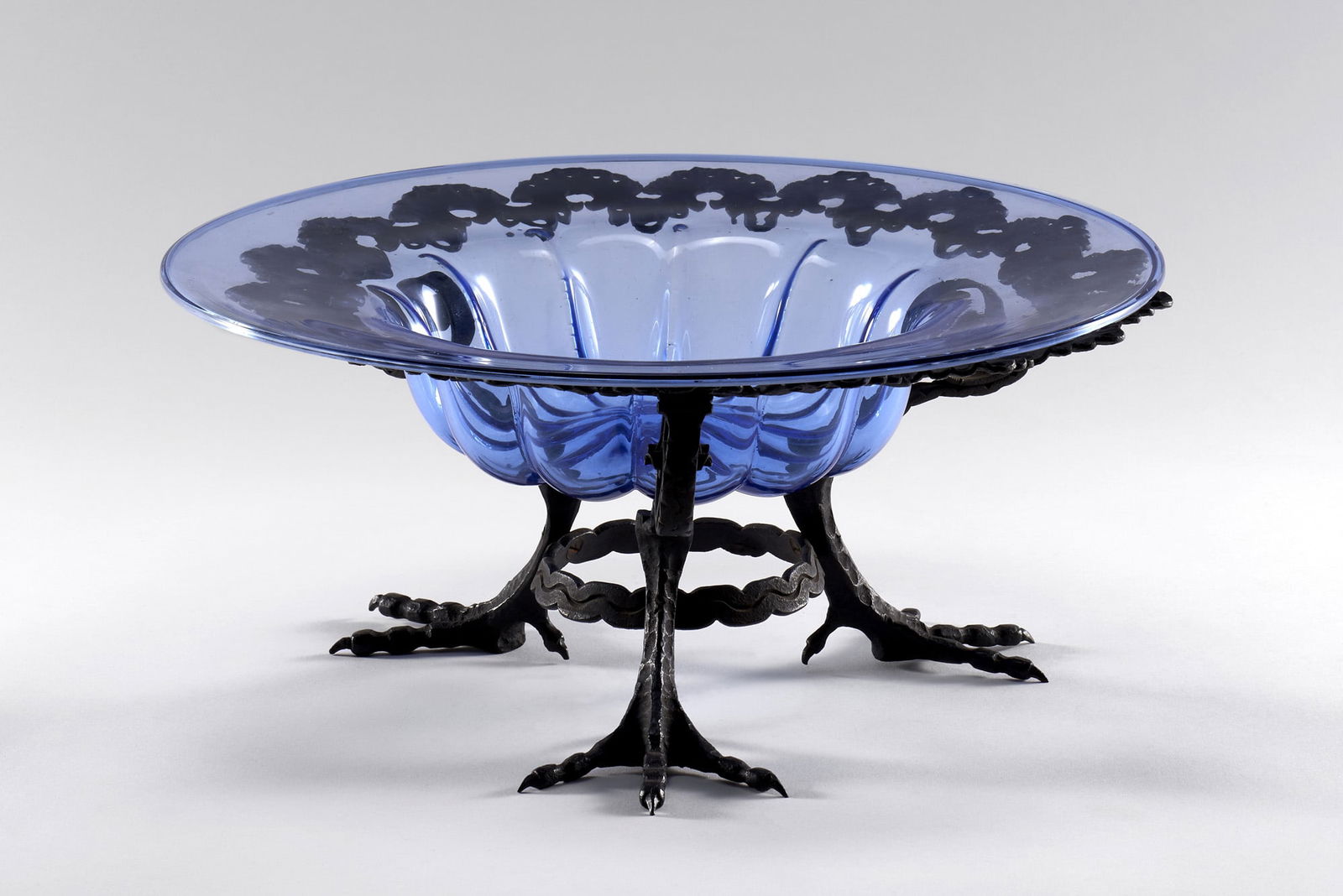 Carlo Rizzarda (Feltre 1883 - 1931) Tripod centerpiece. Milan/Murano, 1924-25ca. Wrought iron frame: Carlo Rizzarda (Feltre 1883 - 1931) Tripod centerpiece. Milan/Murano, 1924-25ca. Wrought iron frame and hot-worked sheet metal. Bird's foot legs. Transparent blue blown glass dish made by the VSM Capp