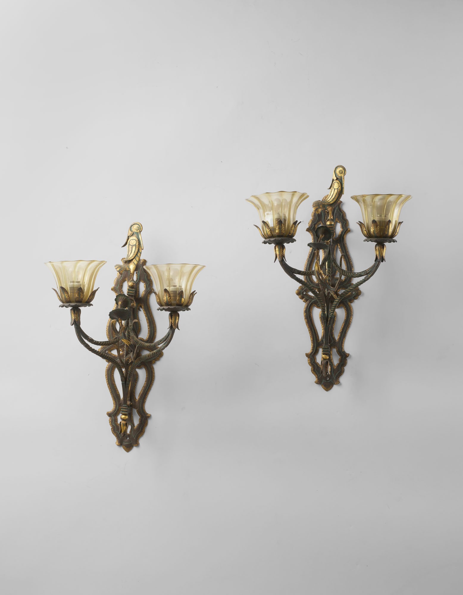 Carlo Rizzarda (Feltre 1883 - 1931) Pair of two-light wall lamps in wrought iron with green and gold: Carlo Rizzarda (Feltre 1883 - 1931) Pair of two-light wall lamps in wrought iron with green and gold patina, decorated with leaves and topped with a bird figure, with ribbed and iridescent glass diffu