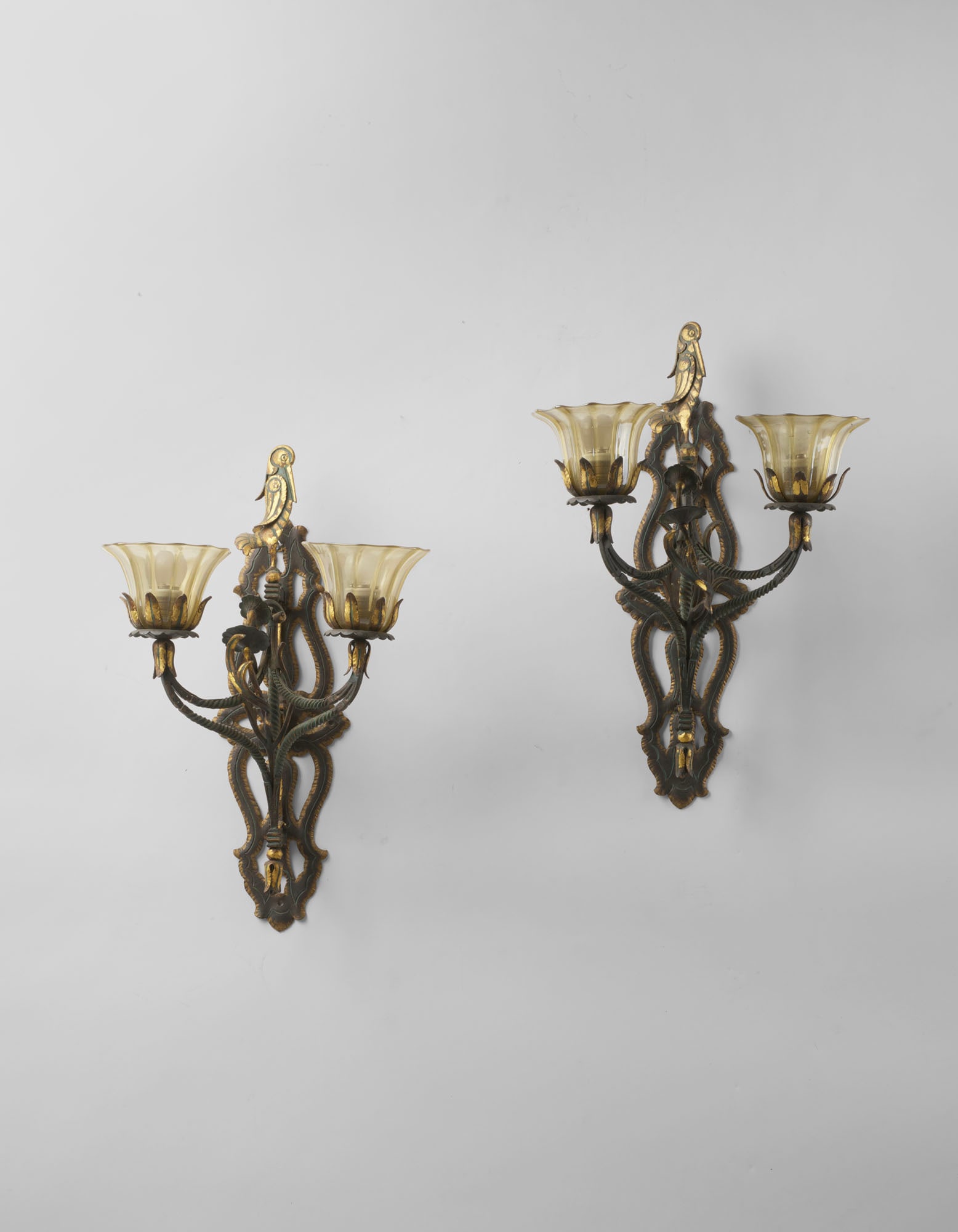 Carlo Rizzarda (Feltre 1883 - 1931) Pair of two-light wall lamps in wrought iron with green and gold: Carlo Rizzarda (Feltre 1883 - 1931) Pair of two-light wall lamps in wrought iron with green and gold patina, decorated with leaves and topped with a bird figure, with ribbed and iridescent glass diffu