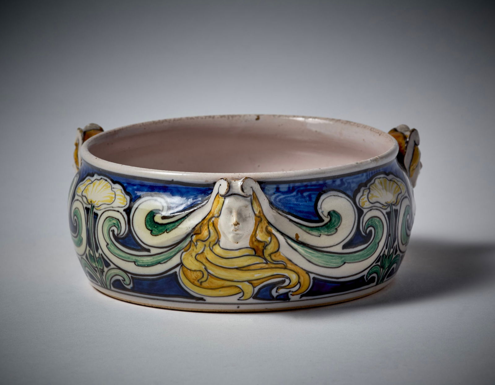 Galileo Chini (Firenze 1873 - 1956) Majolica ceramic bowl decorated with three female heads in: Galileo Chini (Firenze 1873 - 1956) Majolica ceramic bowl decorated with three female heads in relief and painted under glaze with flowers and plant clusters. Manufacture of Arte della Ceramica, Flore