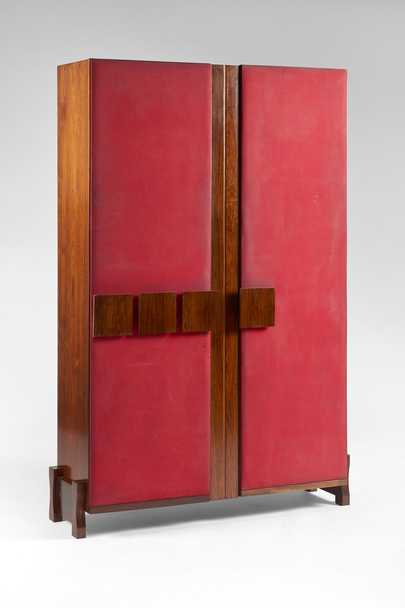 Entrance wardrobe cabinet. Italy, 1960s. Solid wood and veneer, upholstered in red vinyl fabric. Two: Entrance wardrobe cabinet. Italy, 1960s. Solid wood and veneer, upholstered in red vinyl fabric. Two asymmetrical doors, three square wooden handles, protruding side legs. (115x174.5x35.5 cm.) (defect