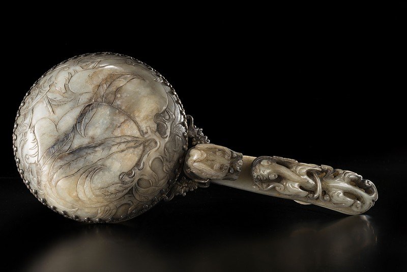 A silver-mounted jade hand mirror. The white and: A silver-mounted jade hand mirror. The white and greyish nephrite carved with two bats perched on peaches, well-wishing symbols of happiness and long life (fu shou shuang quan) China, 20th century (cm
