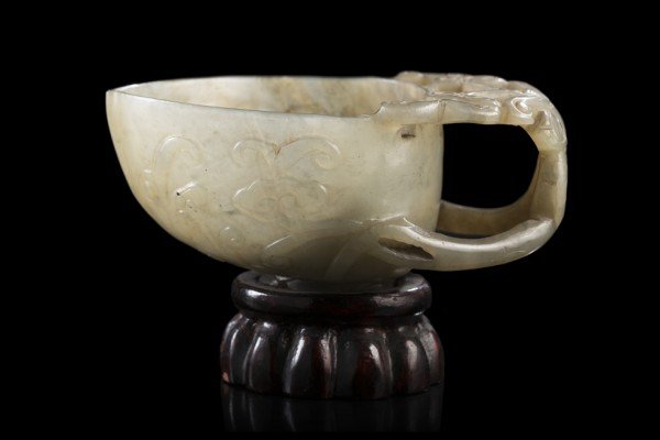 A grey and celadon jade libation cup, the handle carved: A grey and celadon jade libation cup, the handle carved and pierced with ruyi heads, with wood base China, late Ming dynasty (1368-1644) (l. cm. 11)