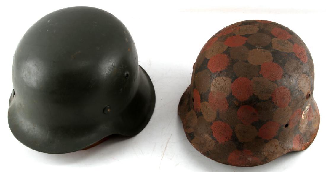 2 WWII M42 GERMAN MILITARY HELMETS ONE DBL DECAL: The first helmet is painted with red, brown, and beige dots with rough texture. On the right side is an SS decal and the other has a very worn off swastika in shield decal. Number to rear is 20775, an