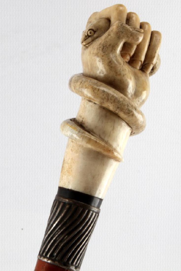 ANTIQUE BONE FIST GRASPING SERPENT WALKING STICK: Well done hand carved bone grip, horn spacer and sterling wrap, some moderate wear to shaft with original ferrule tip, measures 34 inches. Face, Dial, Hands: john This lot has a reserve.