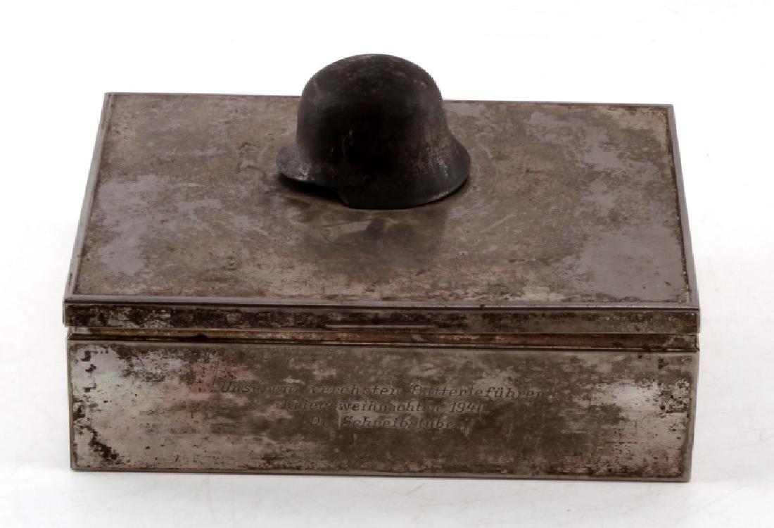 WWII GERMAN MILITARY INSCRIBED TRINKET BOX: Silver colored trinket /cigar box with wooden interior. Small three-dimentional iron (?) soldier hat on top. front of box has long inscription and is dated 1940. panel on bottom is loose. Tarnish is p