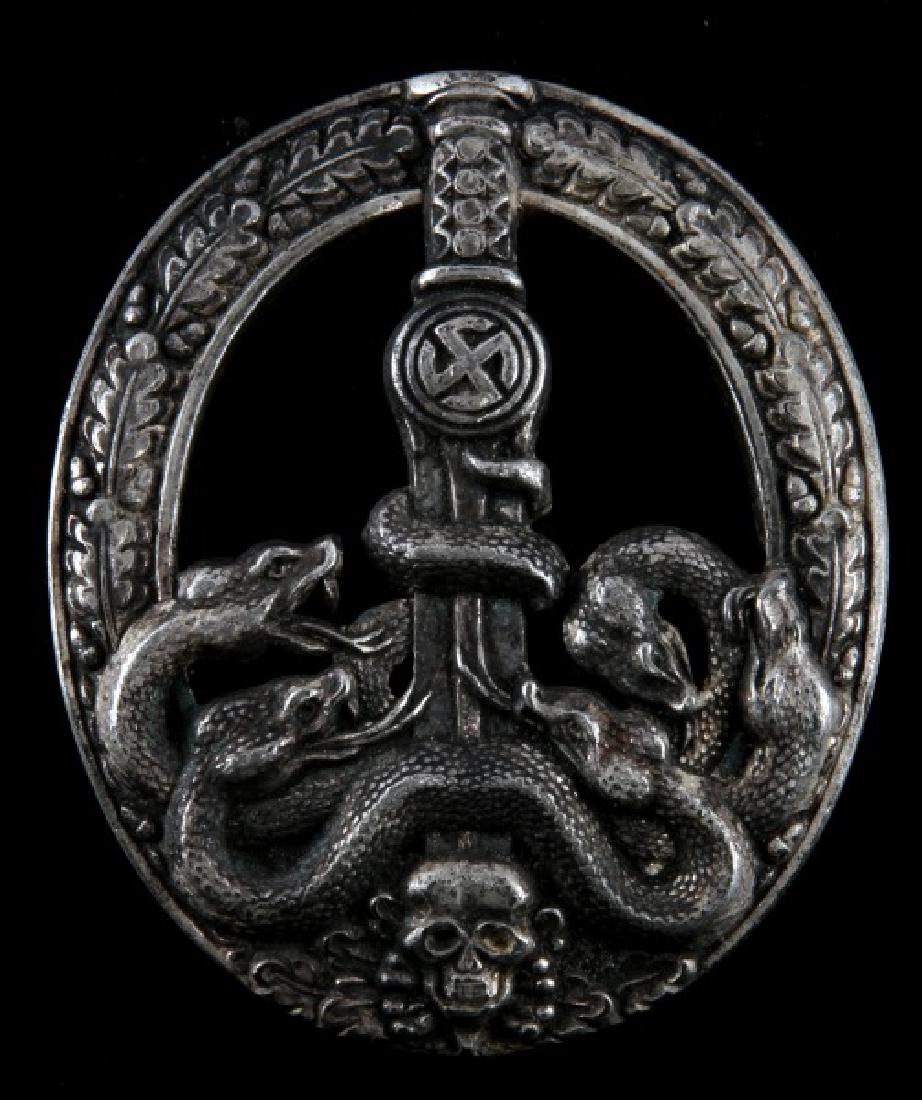 GERMAN WWII ANTI PARTISAN BADGE SILVER 2ND CLASS: German WWII Anti-Partisan Badge in Silver. First type hollow stamped version. Partial open oak leaf wreath holding a relief sword/sun-wheel swastika, intertwined snakes and a skull/crossbones. Fine de