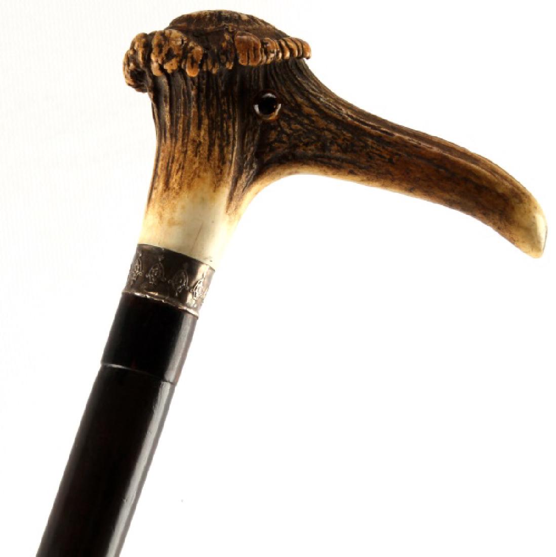 ANTIQUE STAG ANTLER ZOOMORPHIC CANE WALKING STICK: Antique walking stick with a stag antler handle. The handle has a pair of glass bead eyes which give it the appearance of having a bird's head and beak. Silver collar, with a polished wooden handle, a