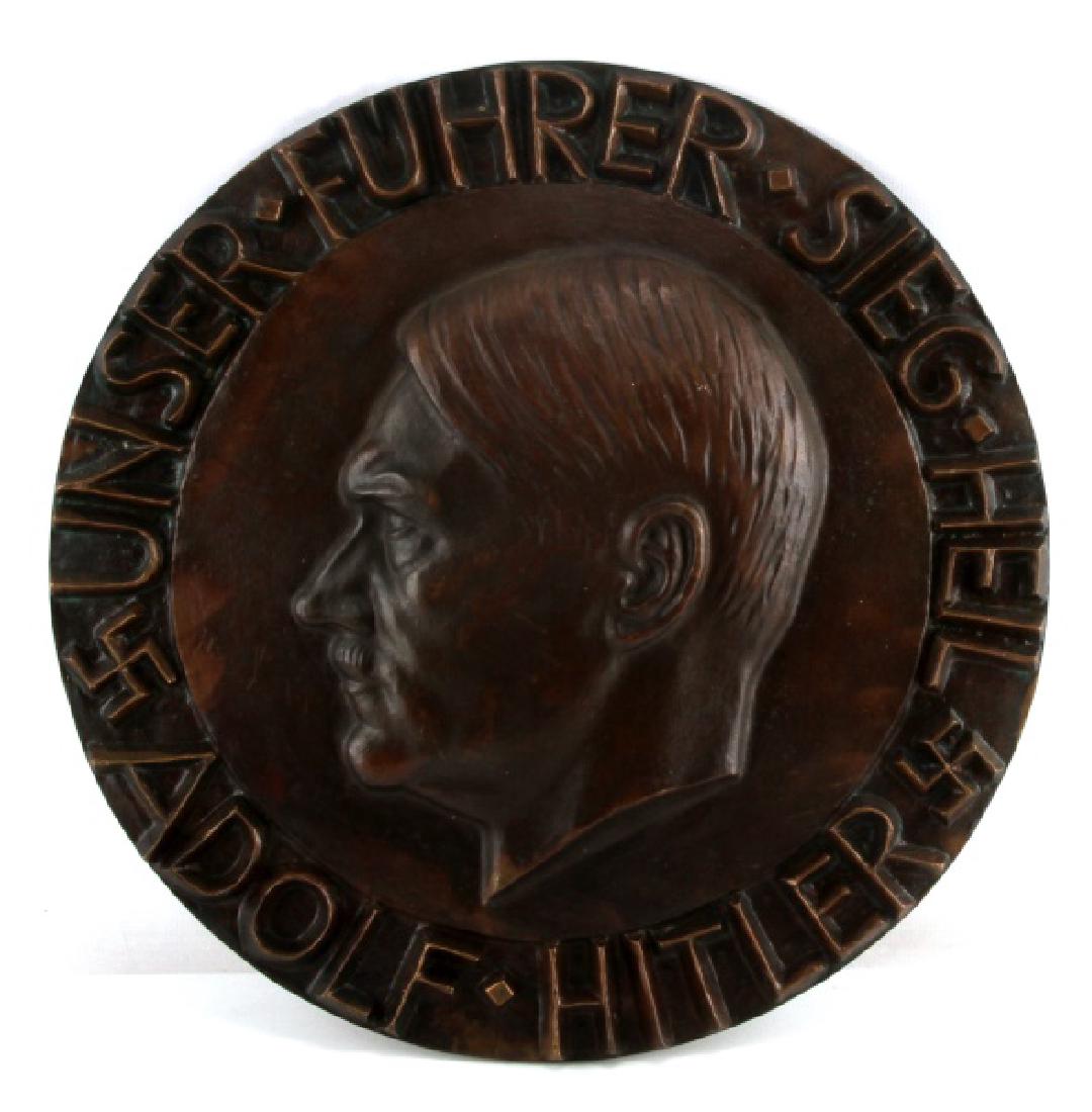 ADOLF HITLER BRONZE MEDALLION PLATE HANGER: With the letters and profile of Hitler in relief, "Unser Fuhrer Sieg Heil Adolf Hitler" (Our leader won). Hanger to back. Very good condition. Weighs 19 pounds. Measures 18 inches in diameter.