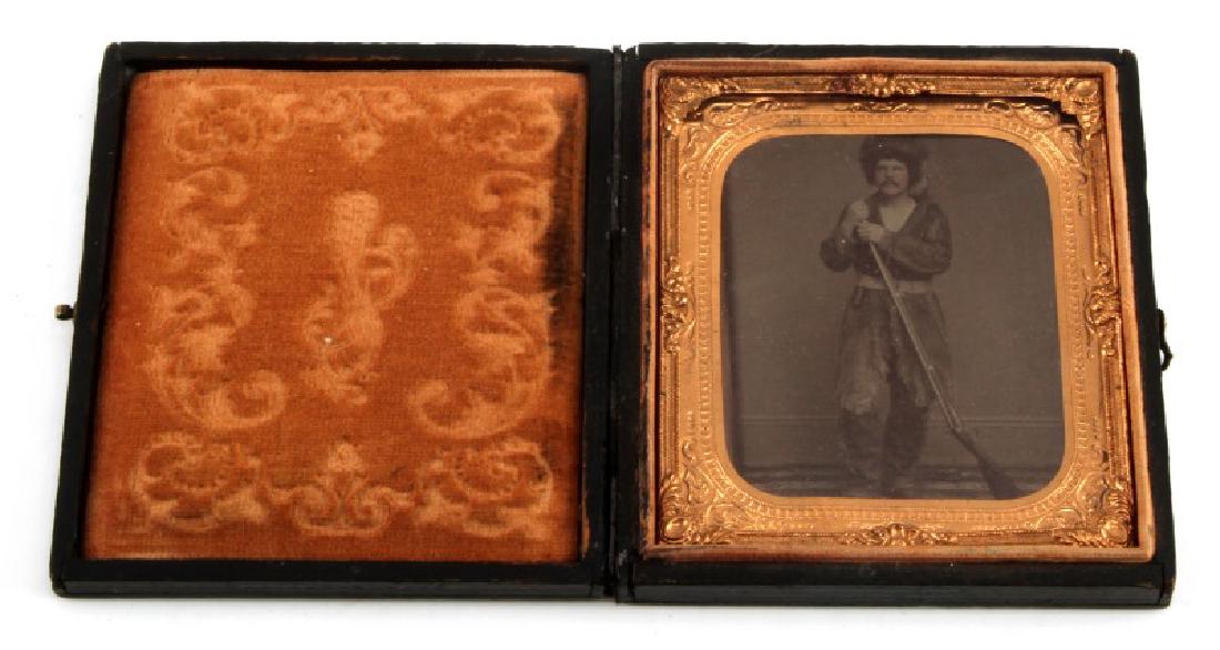1/6 PLATE TINTYPE OF BUCKSKIN & RIFLE FRONTIERSMAN: Fur hat, knife, percussion rifle and pistol in buckskin, i very good union case measuring 3.25 by 3.5 inches.