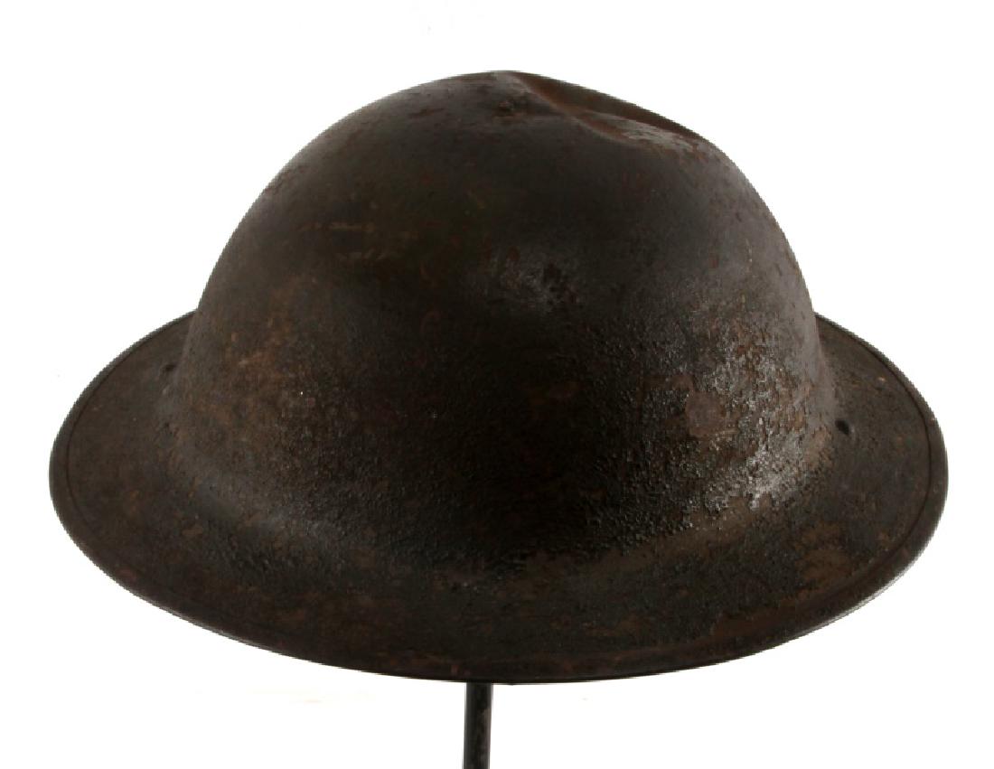 WWI BRITISH BATTLE DAMAGED STEEL BRODIE HELMET: Steel Brodie helmet, probably a Mark I based upon the magnetic rim, with a large dent on the top of the helmet and a small hole punctured into the front of the helmet. In good condition with some pitt