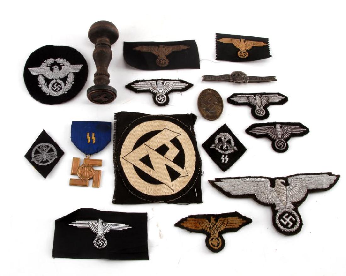 LOT OF GERMAN WAFFEN SS PATCHES MEDALS DISC STAMP: Lot of German Waffen SS items. Includes Totenkopf breast pin that features RZM stamp and M1/34 stamp, Berlin Police Warrant/Gestapo disc, Long Service Medal with ribbon, wooden hand stamp, officers sl