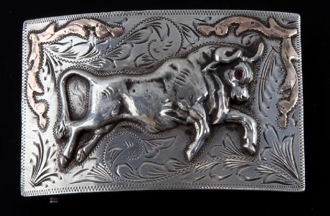 STERLING SILVER SOUTHWESTERN STYLE BELT BUCKLE: Stamped Sterling Mexico on reverse. Obverse features charging bull with ruby eye, hand tooling and some rose gold overlay. Measurements are 2 1/8 by 3 3/4 inch.